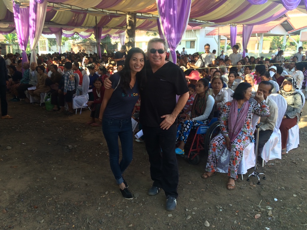 Steve Bender and a volunteer in front of hundreds of patients seated under a large tent