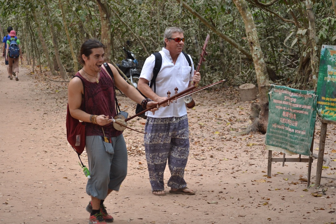 Steve Bender and a team member laugh as they carry Khmer fiddles past the band's sign, Traditional music by victims of landmine