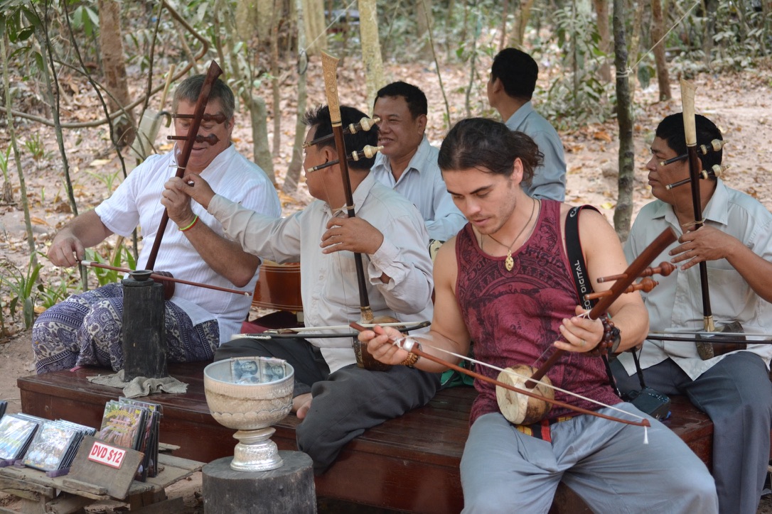 Steve Bender and a young team member play traditional Khmer string instruments alongside members of a landmine survivors band