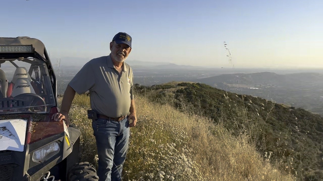 A man in a Rotary cap standing on a hilltop at sunset above the valley